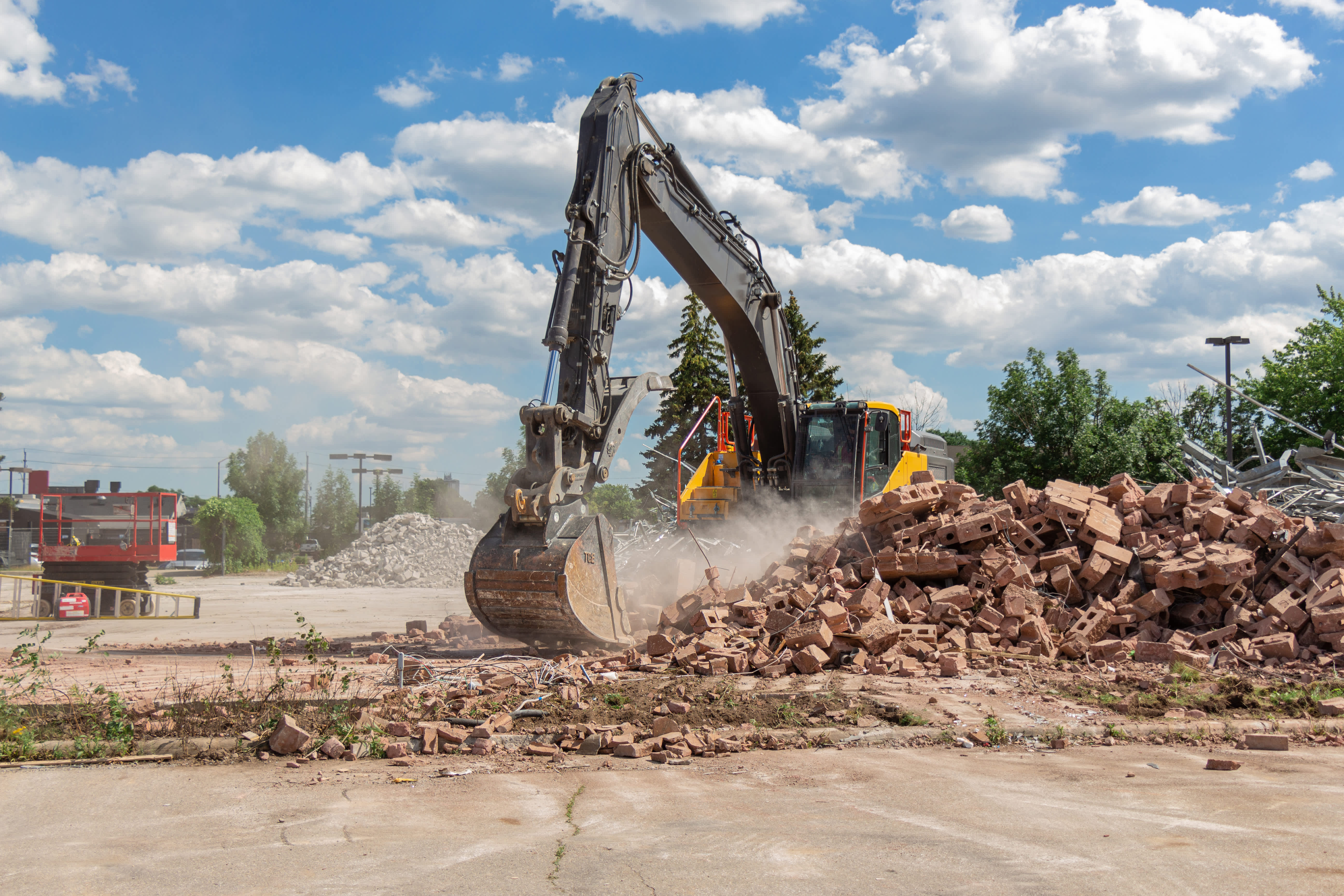 excavator rental on demolition site digging debris with dust flying